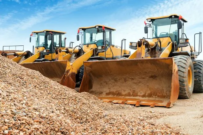 Three large orange and black excavators parked next to each other in front of a pile of rubble on a sunny day.
