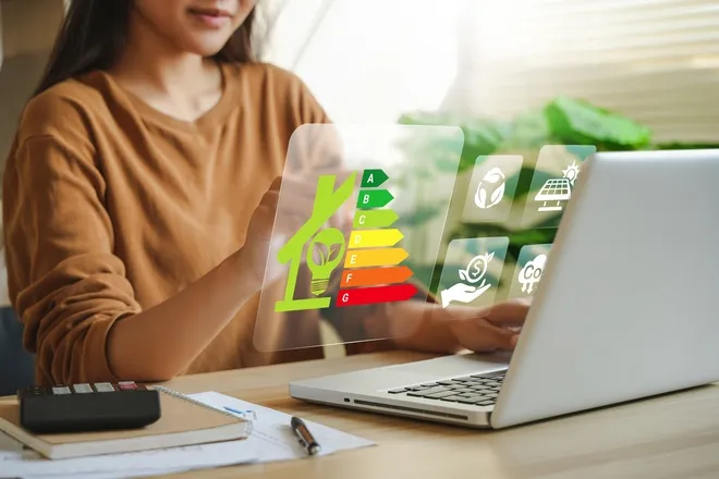 A woman sits at a desk on her laptop while she uses her left hand to interact with a graphic of charts and letters.