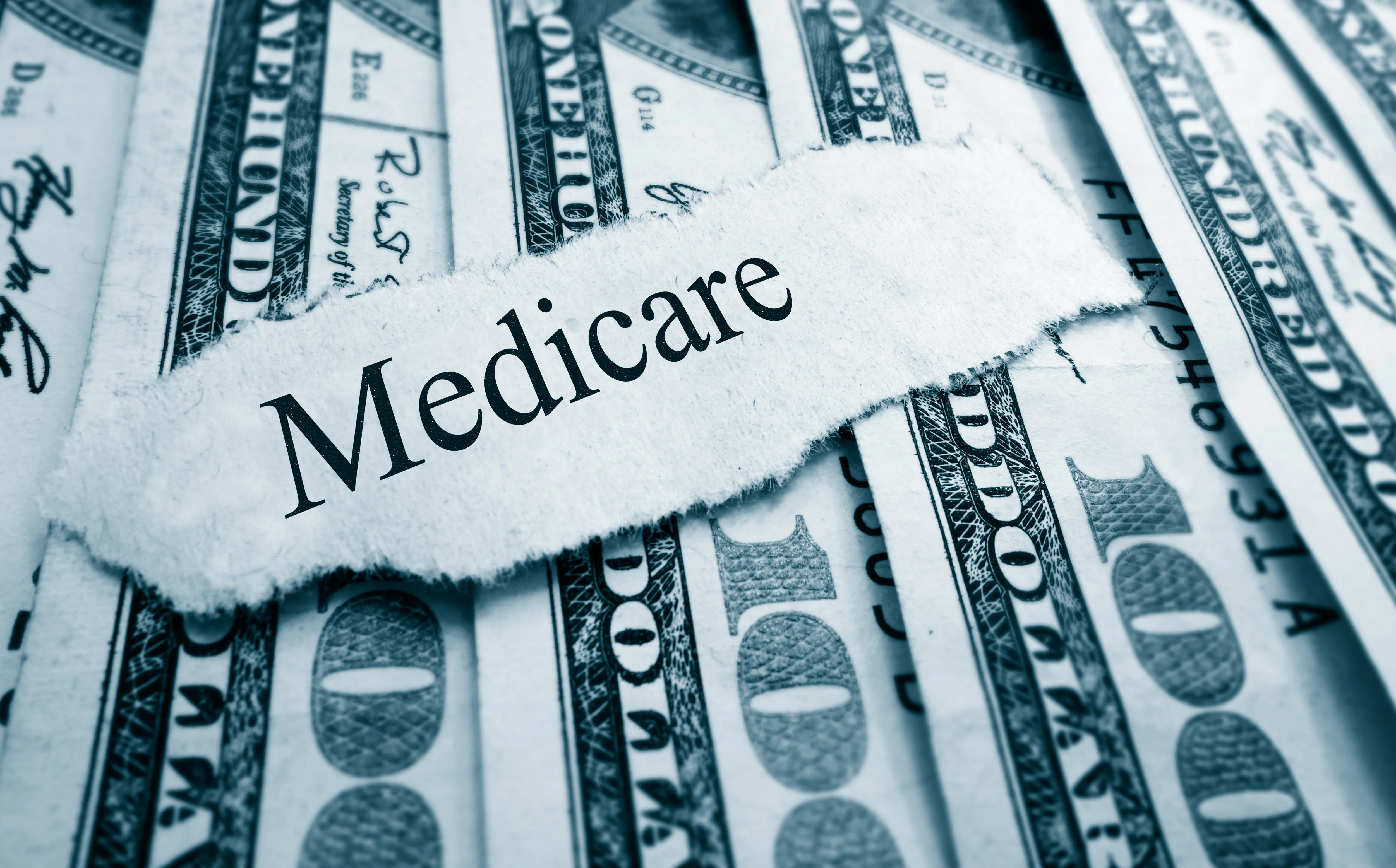 A scrap of torn paper with the word "Medicare" rests on top of a spread of United States 100 dollar currency.