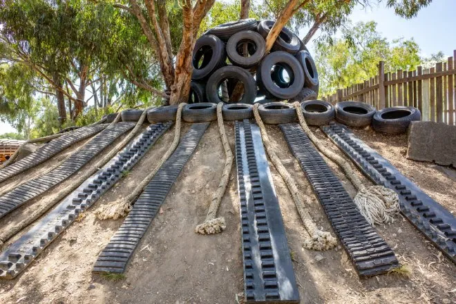 An outdoor play space with recycled materials, such as tires, rope, and metal hardware. The play space is on a dirt incline.