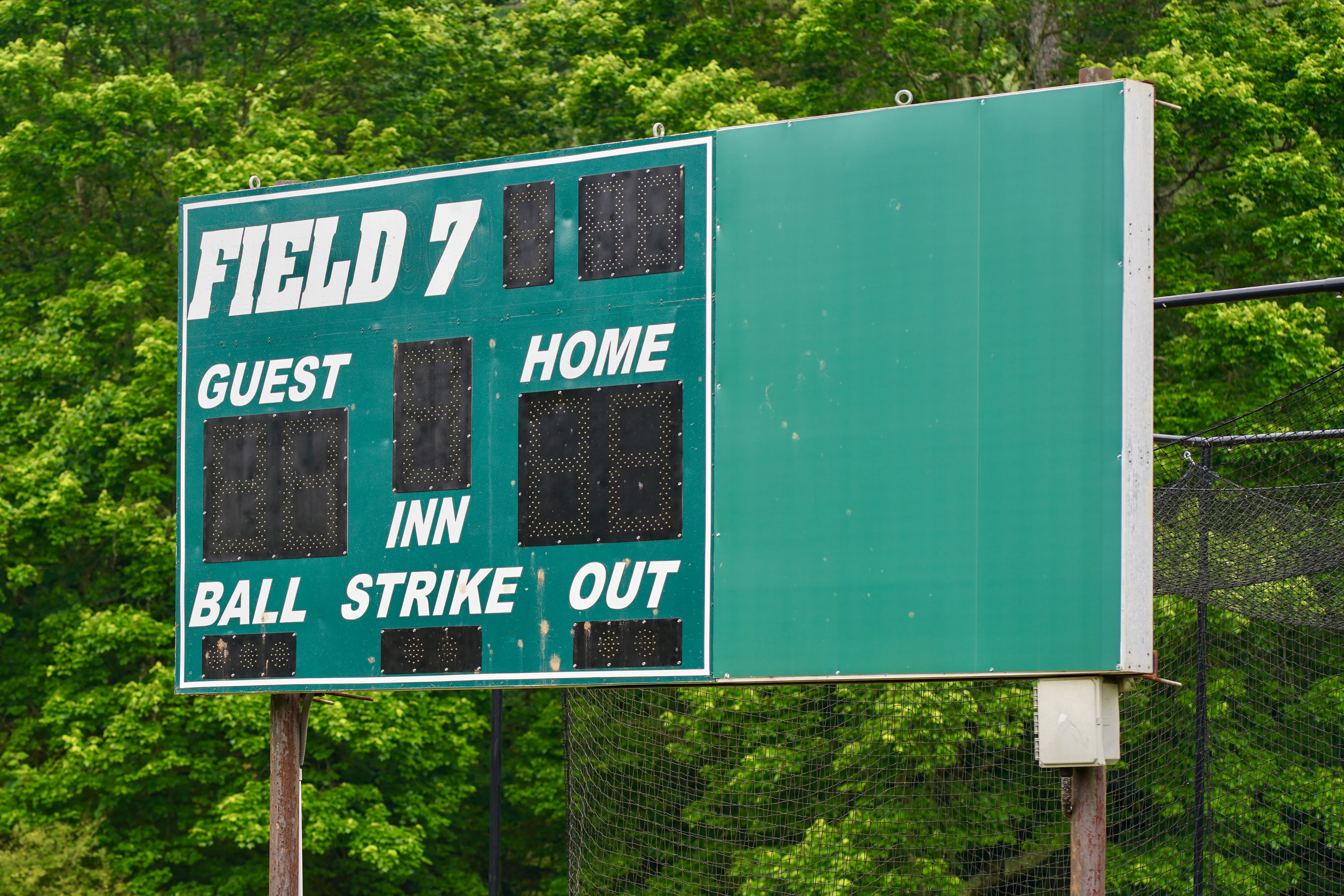 Baseball or softball scoreboard in front of trees.