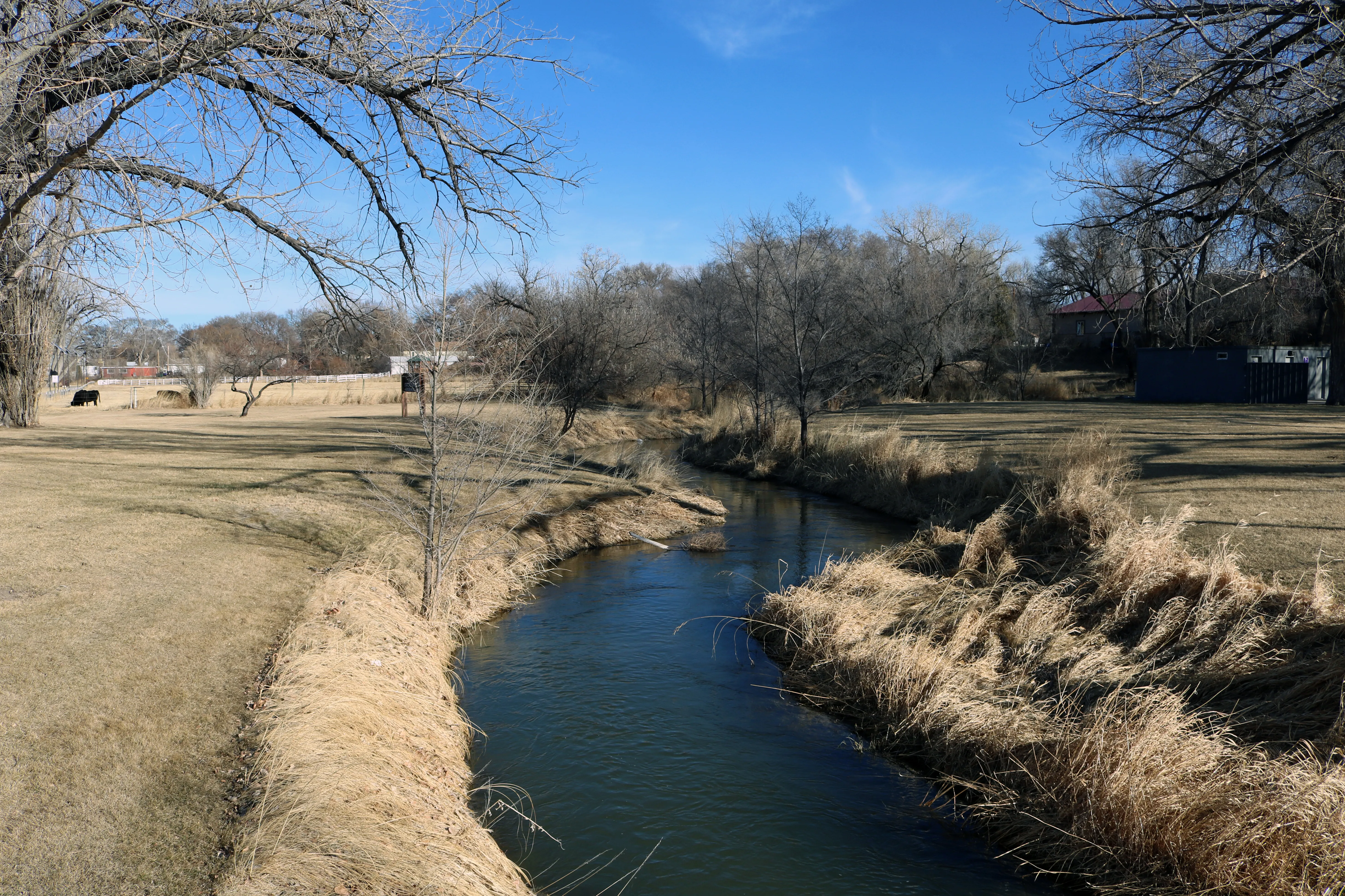 View of a small river winding through an open area with trees in the distance.