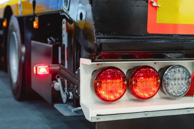 A close-up of one of a semitrailer's taillights. All three red lights, including one protruding on a metal prong, are lit.