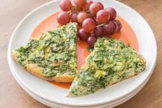 French Spinach Frittata Small stack of plates with two slices of spinach frittata and a small group of grapes.