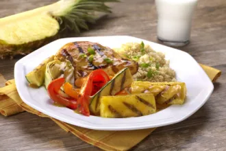 Plate of Grilled Pineapple Ginger Glazed Chicken on a table with a glass of milk and half of a pineapple in the background.