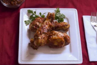 Spicy Southern Barbeque Chicken - USDA Square plate with pieces of spicy southern barbecue chicken on a wood table next to a fork on a napkin.