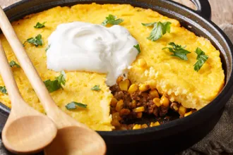 Stovetop Tamale Pie - USDA Skillet of stovetop tamale pie topped with sour cream with two wooden serving spoons and a slice removed.