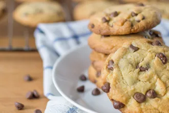 Chocolate Chip Yogurt Cookies - USDA Plate of chocolate chip yogurt cookies on a dish towel, next to a few individual chocolate chips and a wire cooling rack of cookies.