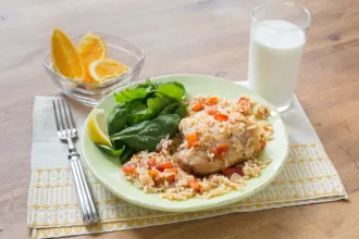 Arroz Con Pollo - USDA Table with a placemat under a plate of chicken and rice with spinach leaves and a lemon wedge next to a fork, glass of milk, and bowl of lemon or orange wedges.