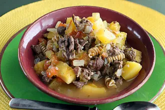 Hearty Beef Soup - USDA Bowl of hearty beef soup on a plate next to a spoon.
