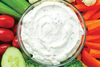 Overhead image of a bowl of low fat ranch dip surrounded by fresh vegetables.