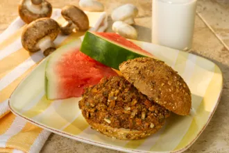 Mushroom Beef Sloppy Joes - USDA Mushroom beef sloppy Joe on a square plate with two quarter slices of watermelon. Three fresh mushrooms and a glass of milk are in the background.