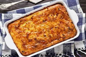 Matzo Meal Kugel - USDA Casserole dish of Matzo Meal Kugel on a cloth next to a serving utensil.