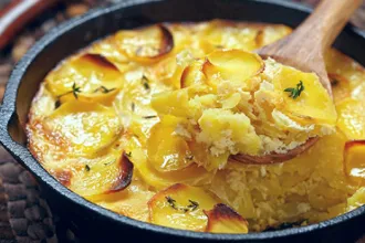 Close up view of a cast iron pan of scalloped potatoes. A wooden spoon presents 