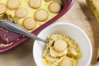 Southern Banana Pudding - USDA Overhead view of a bowl of southern banana pudding with a spoon next to a pan of southern banana pudding with a serving removed.