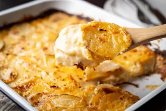 Baking dish of au gratin potatoes with a wooden spoon showing a closer view of the cooked ingredients.
