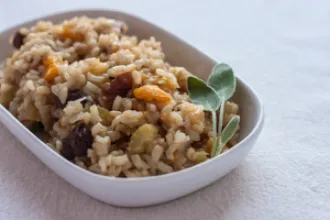 Small rounded rectangular bowl of Brown Rice Pilaf with a sprig of sage in one corner.