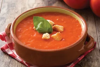 Closeup of a bowl of tomato basil soup sitting on a cloth.